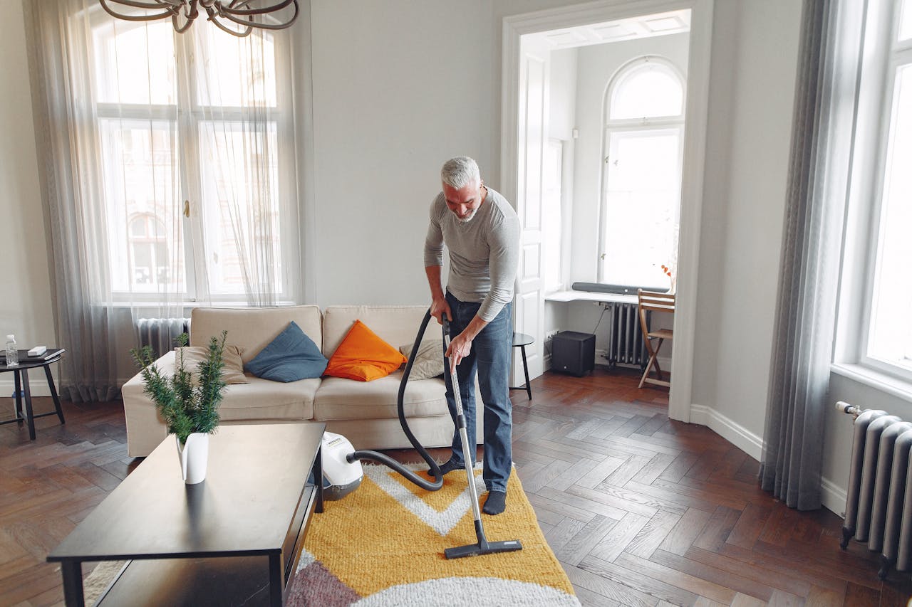 stats-img From above of focused grey haired man with beard vacuum cleaning carpet at home