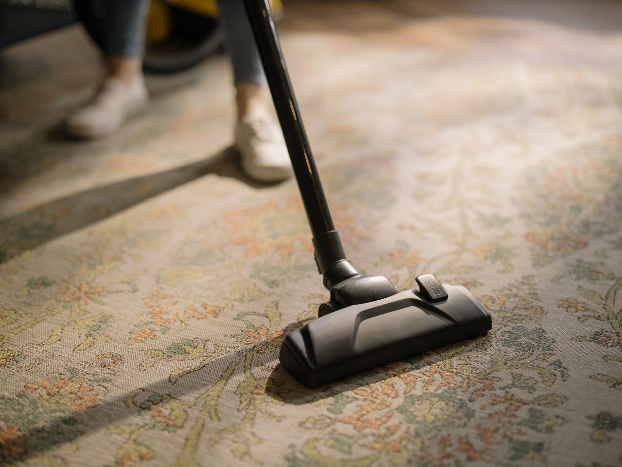 why-choose-us Close-up of a vacuum cleaner on a patterned carpet in a sunlit room, capturing a moment of household cleaning.