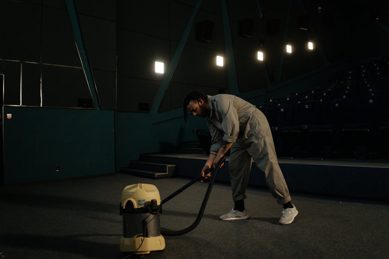 portfolio-05 A cinema employee cleaning the theater floor with a vacuum cleaner under dim lights.